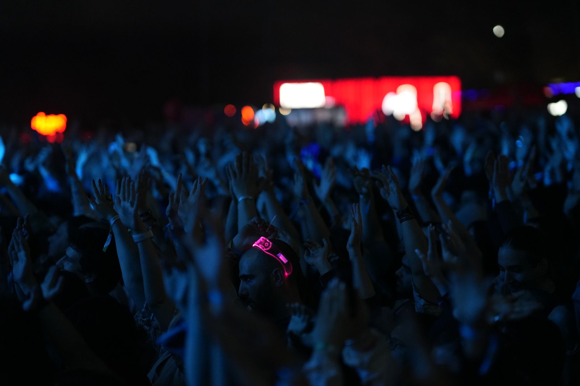 Hundreds of hands raised in blue light in front of a red-lit main stage
