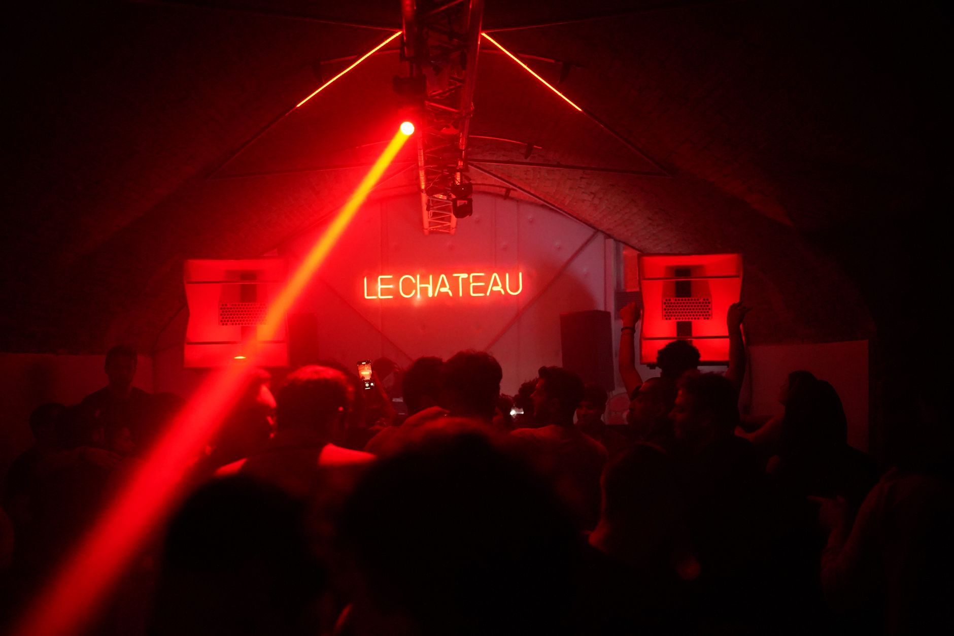 Fans packed under red neon and a single beam of light just inside a venue door