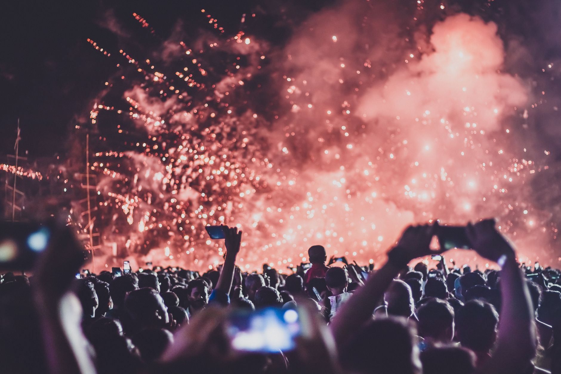 Fireworks bursting over a festival crowd silhouetted against the night sky