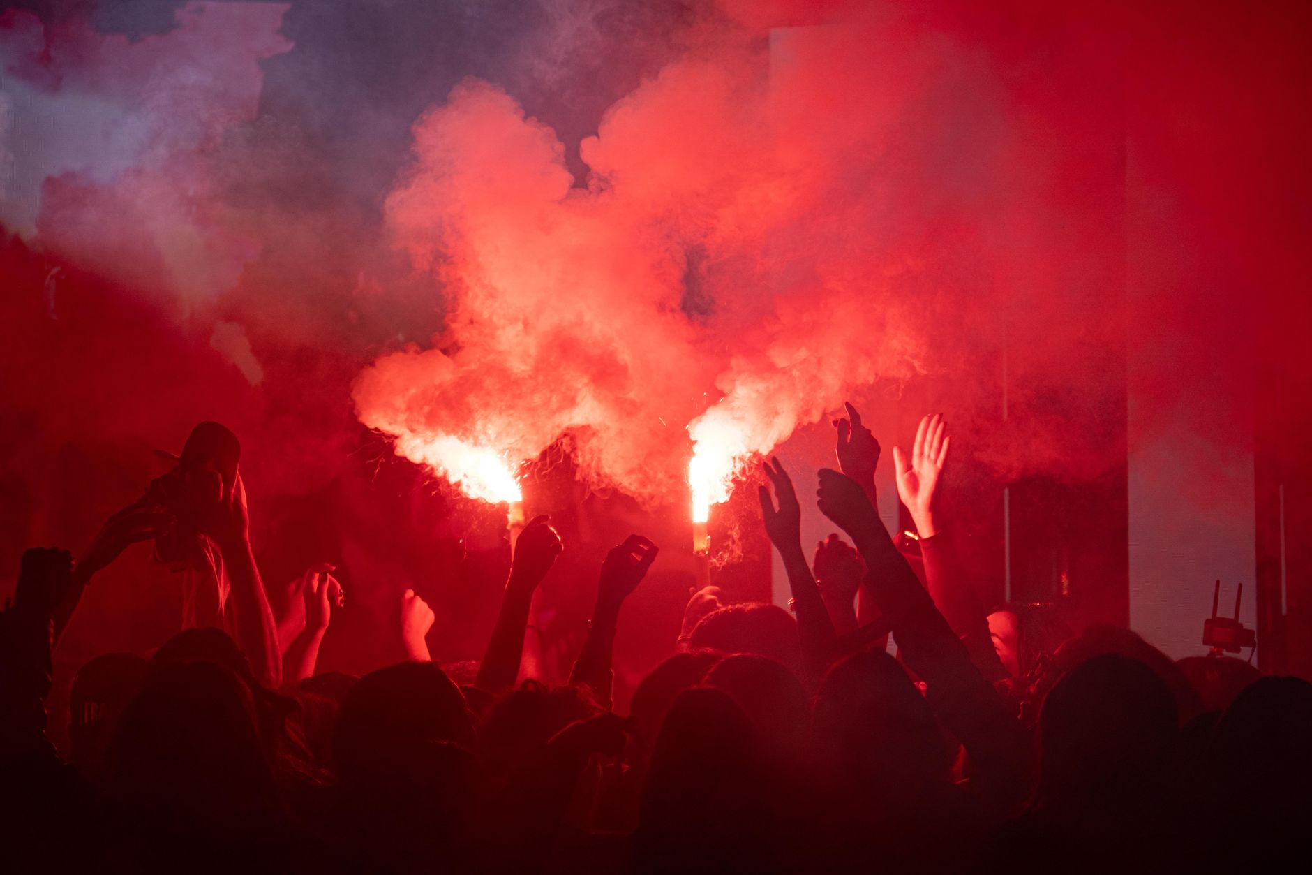 A crowd lit by red flares and smoke at an outdoor night show